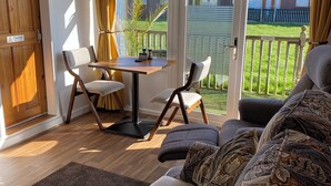 Ein Zimmer mit einer Couch, einem Tisch mit Stühlen, einer Holztür und Blick auf eine Grünanlage.