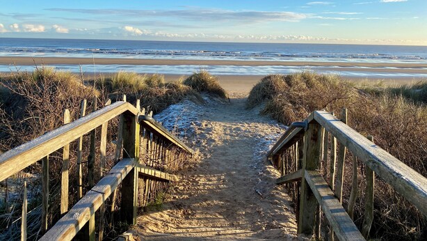 Eine Holztreppe führt zu einem Strand mit freiem Blick auf das Meer.