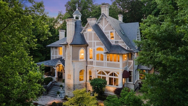 A large, multi-story house with a stone facade, multiple chimneys, and a well-lit interior.