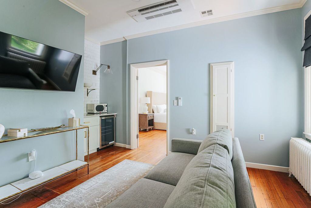 A modern living room with a flat-screen TV, a sofa, a coffee table, and a kitchen area visible through an open door.