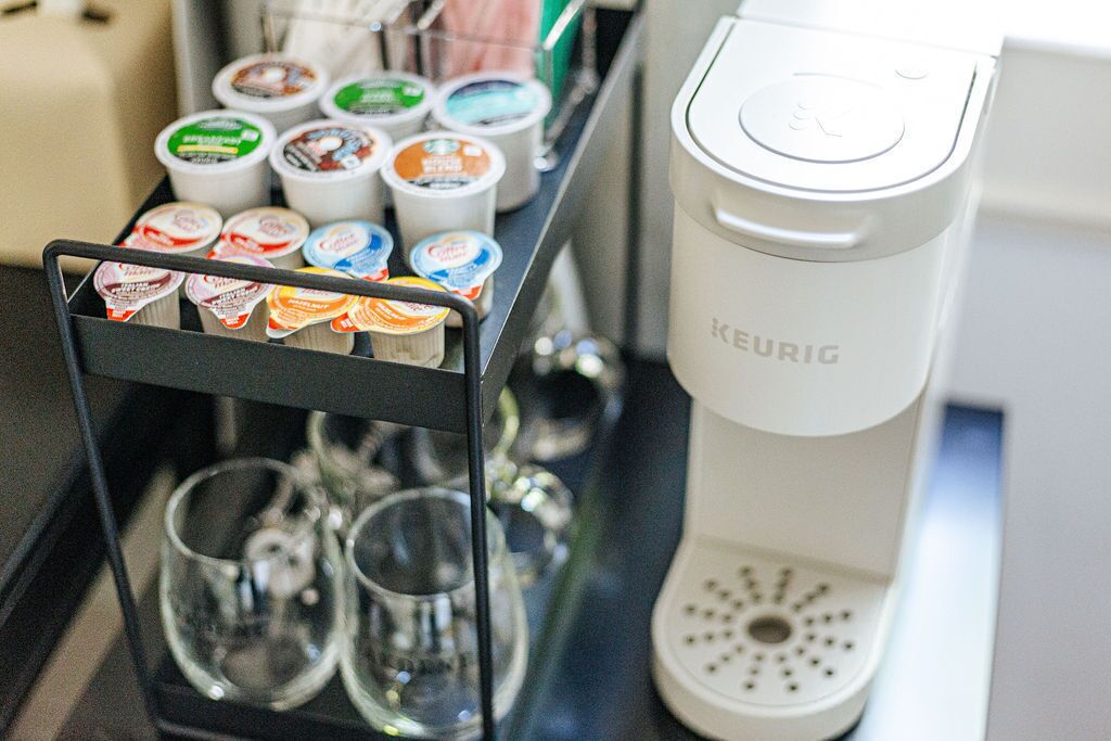 A Keurig coffee maker with a milk frother and a cup holder with various coffee pods.