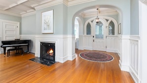 A spacious room with a grand piano, a fireplace, and a large arched doorway leading to another area.
