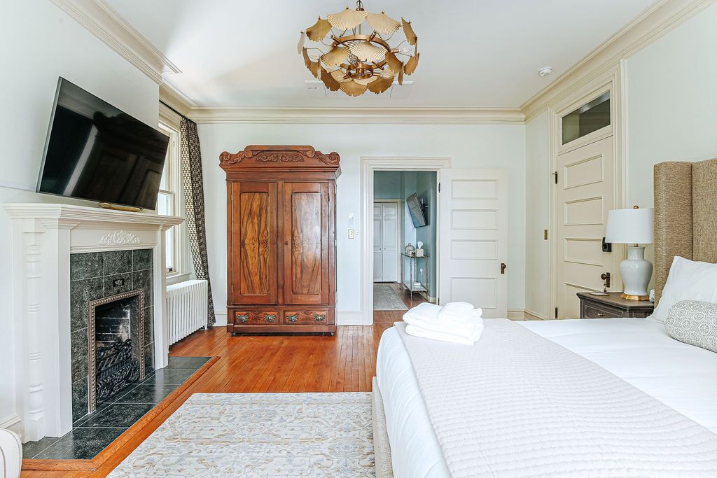 A hotel room with a fireplace, a large bed, a television, and a wooden wardrobe.