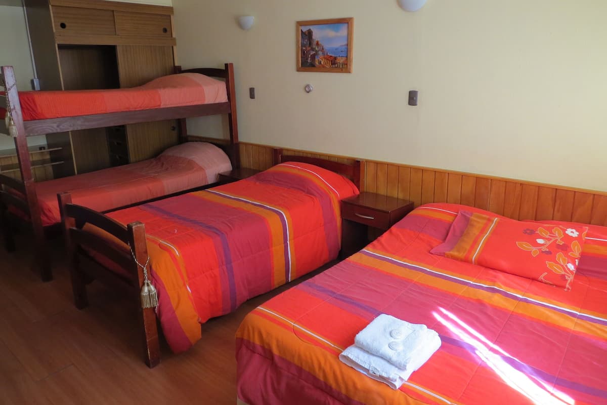 Una habitación con literas y dos camas individuales, muebles de madera, una mesita de noche pequeña y un aplique de pared.