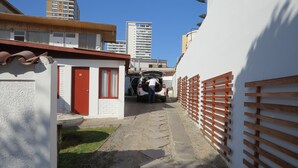 A narrow alleyway with a white building on the left, a red door, and a white building on the right with a wooden fence. - Palm Hostal (Iquique)