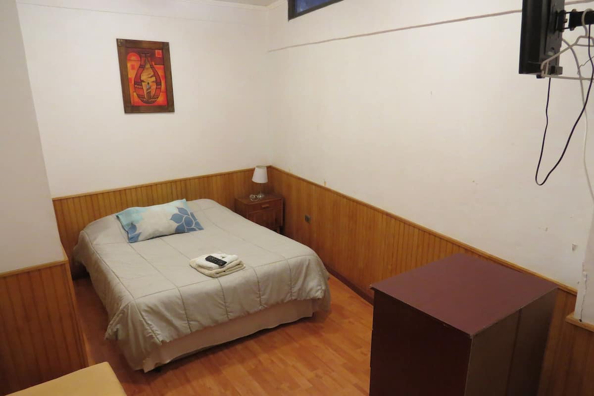 Un dormitorio pequeño y ordenado con cama, mesita de noche, lámpara y mesita auxiliar de madera.