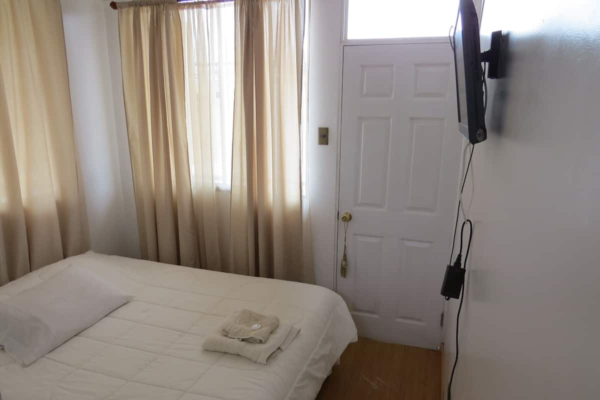 Un dormitorio con cama, cortinas, una puerta y un televisor montado en la pared.