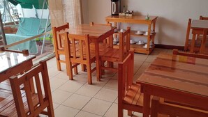 A dining area with wooden tables and chairs, a coffee station, and a cityscape painting on the wall. - Palm Hostal (Iquique)