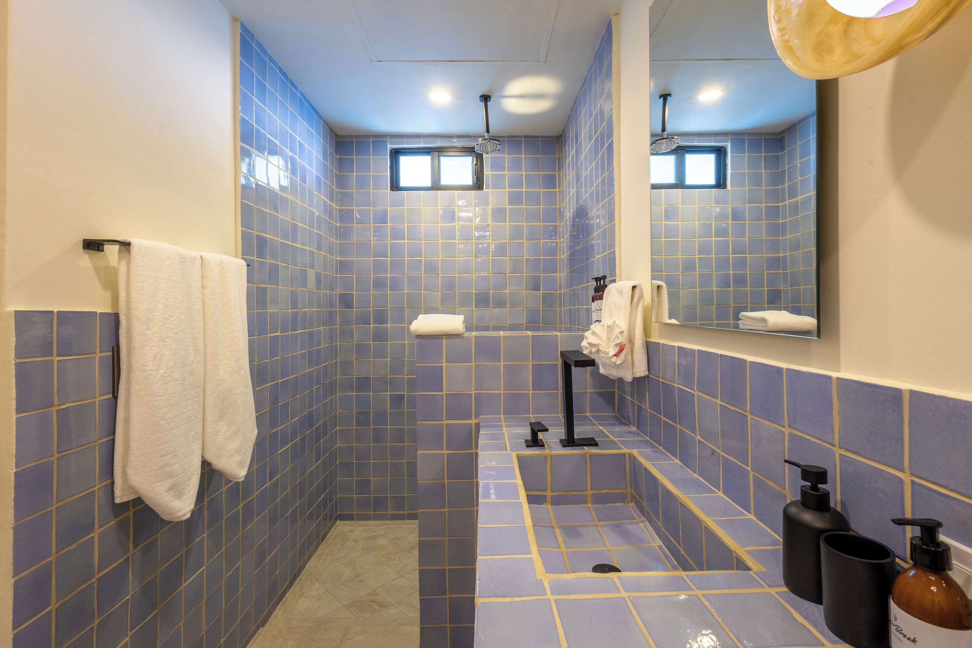A bathroom with blue tiled walls, a white towel hanging on the wall, a sink with a mirror above it, and two bottles of soap on the counter.