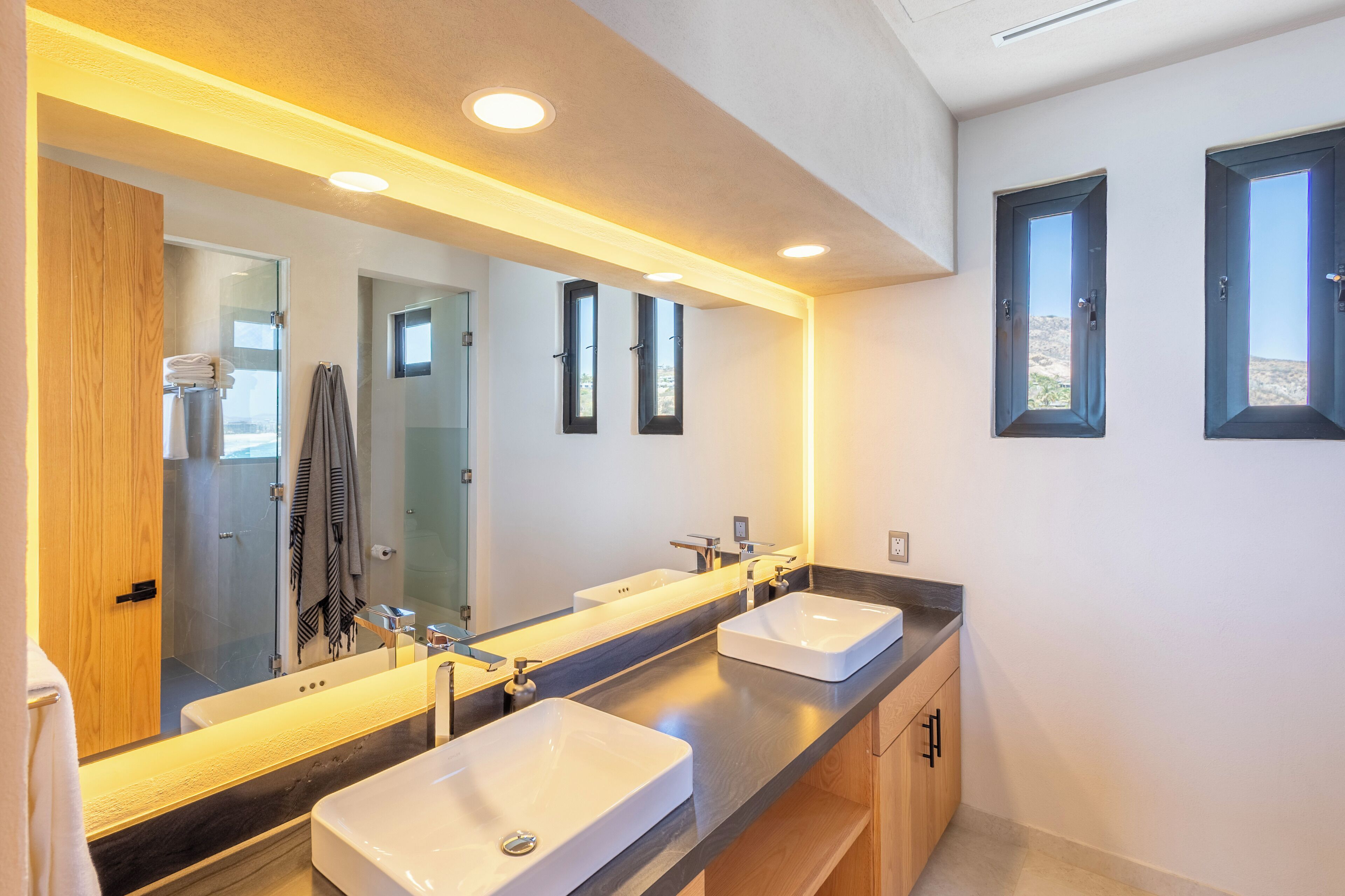 A modern bathroom with two sinks, a large mirror, and a shower area.
