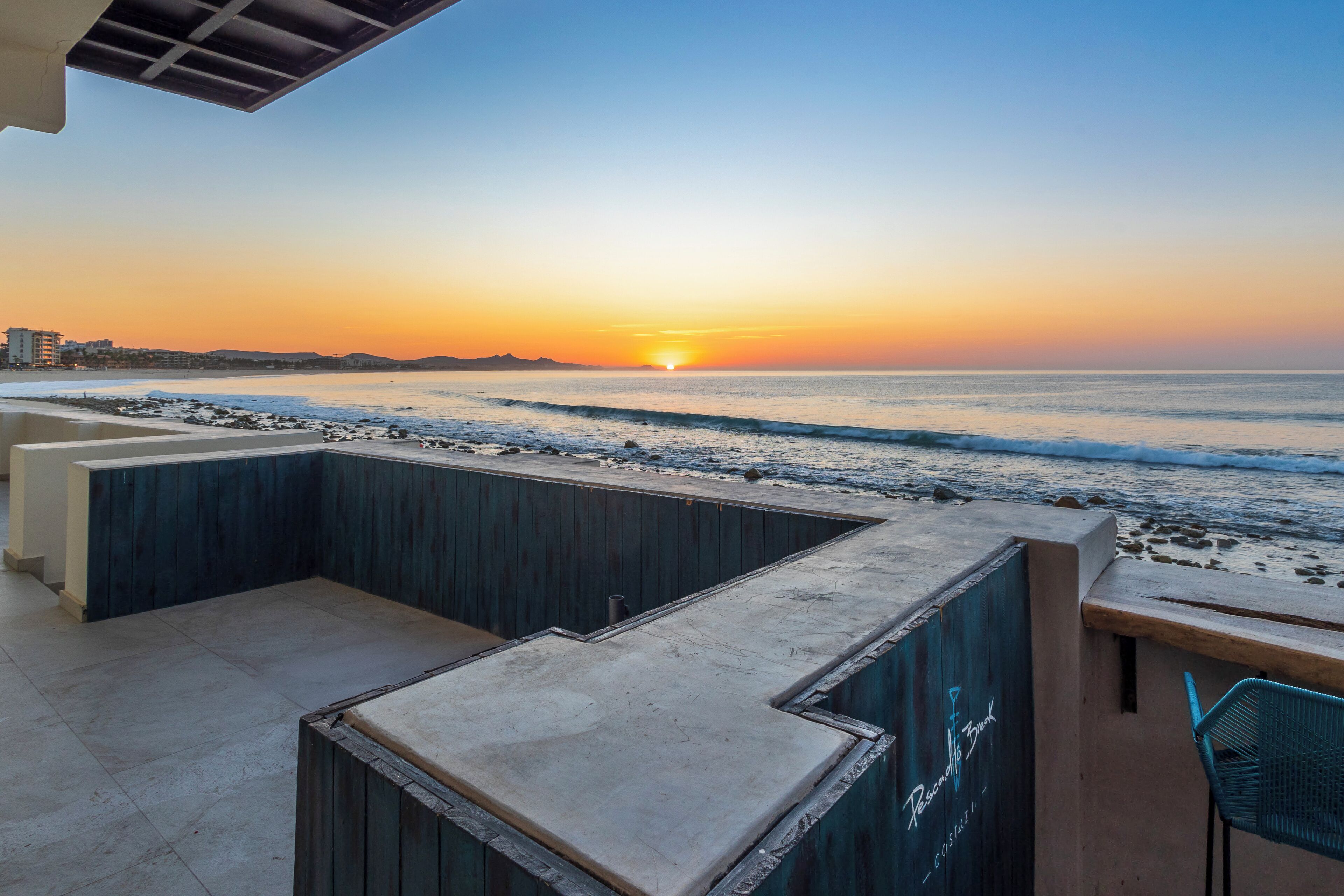 A beachside patio with a view of the sunset over the ocean.