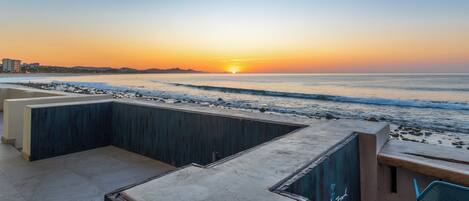 A beachside patio with a view of the sunset over the ocean.
