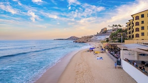 A beach with a sandy shore, a building with a bar, and a rocky hill in the background. - Cabo Break Hotel (San José del Cabo)