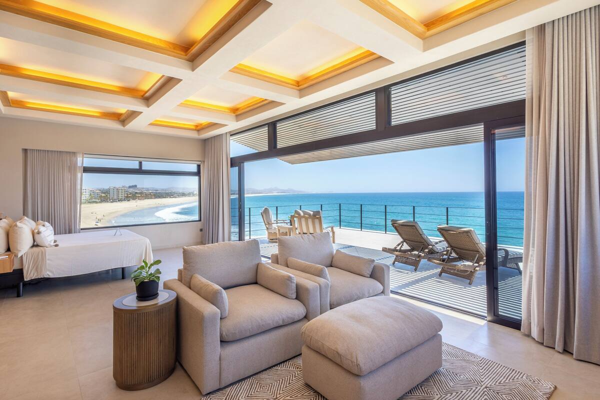 Une chambre d’hôtel moderne dotée d’un grand balcon donnant sur la mer, d’un lit, d’un canapé et d’une petite table d’appoint agrémentée d’une plante.
