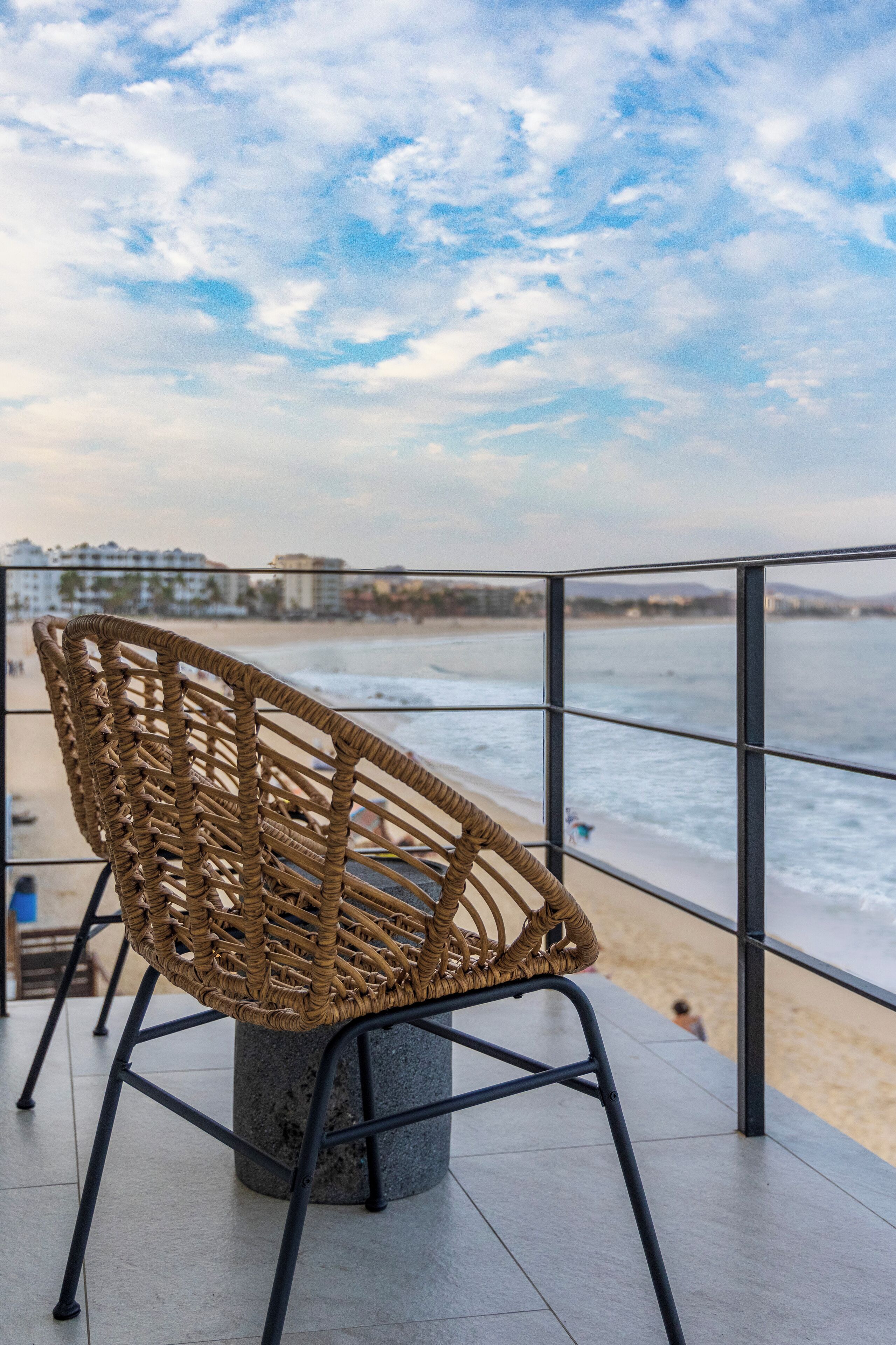Une chaise en osier sur un balcon donnant sur une plage, avec un ciel dégagé.
