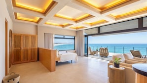 A modern hotel room with a large window overlooking the sea, a wooden partition, a bed, a seating area with a view, and a balcony with a railing. - Cabo Break Hotel (San José del Cabo)