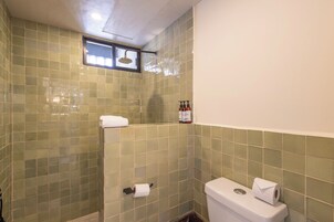 A bathroom with green-tiled walls, a toilet, a shower with a window, and two rolls of toilet paper.