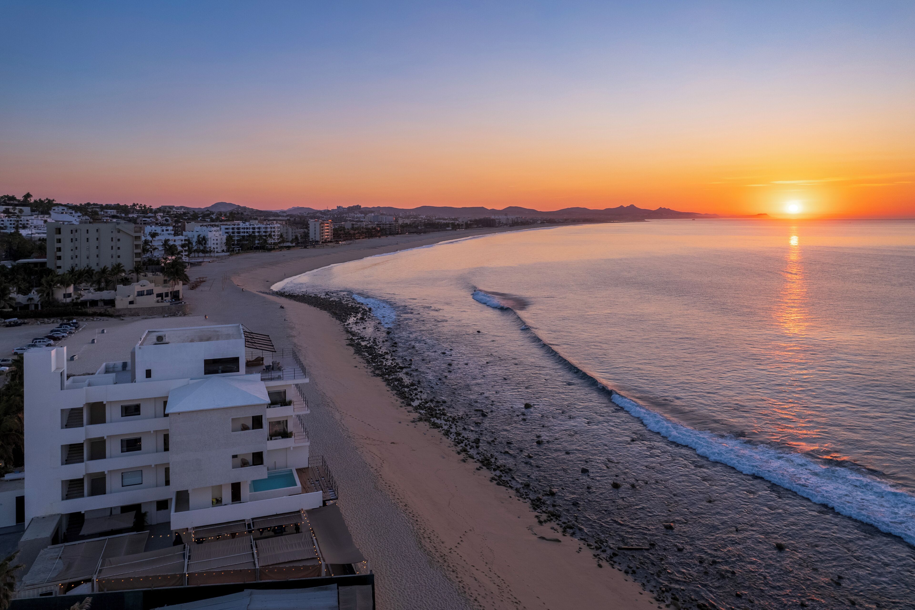 A beachfront hotel with a pool, a beach, and a sunset view.