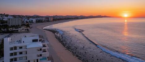 A beachfront hotel with a pool, a beach, and a sunset view.