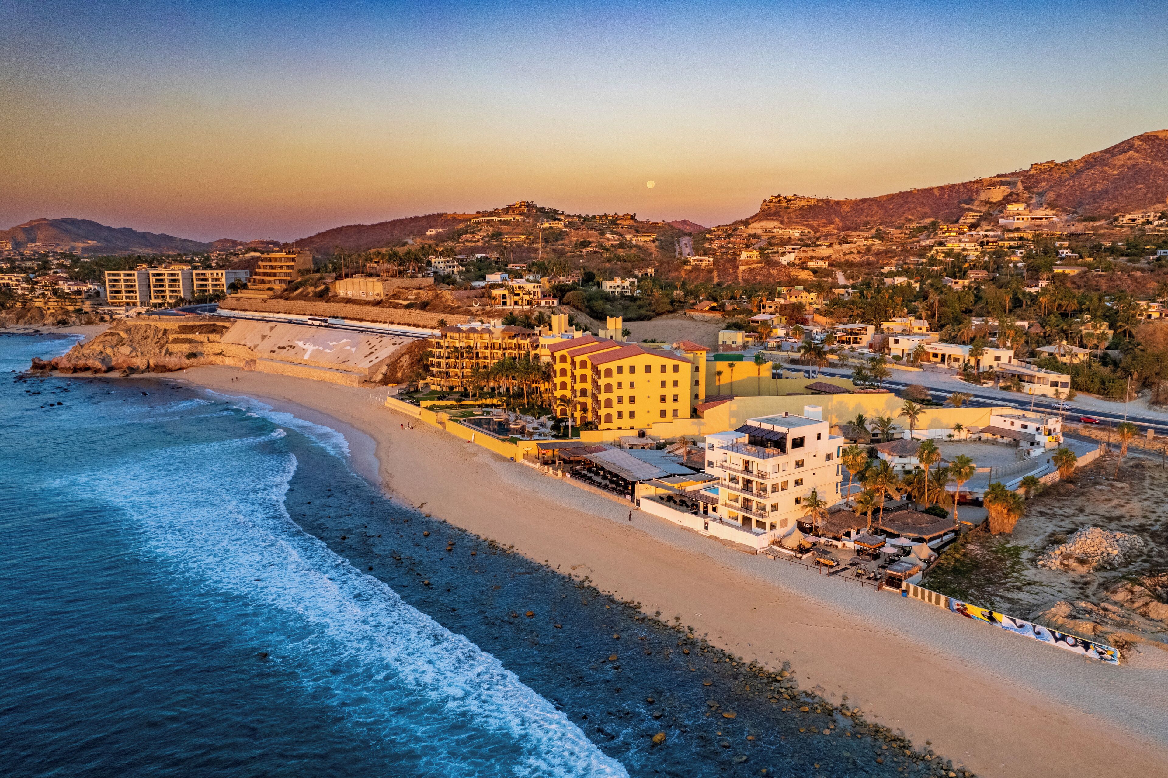 A coastal town with a beach, buildings, and hills in the background.