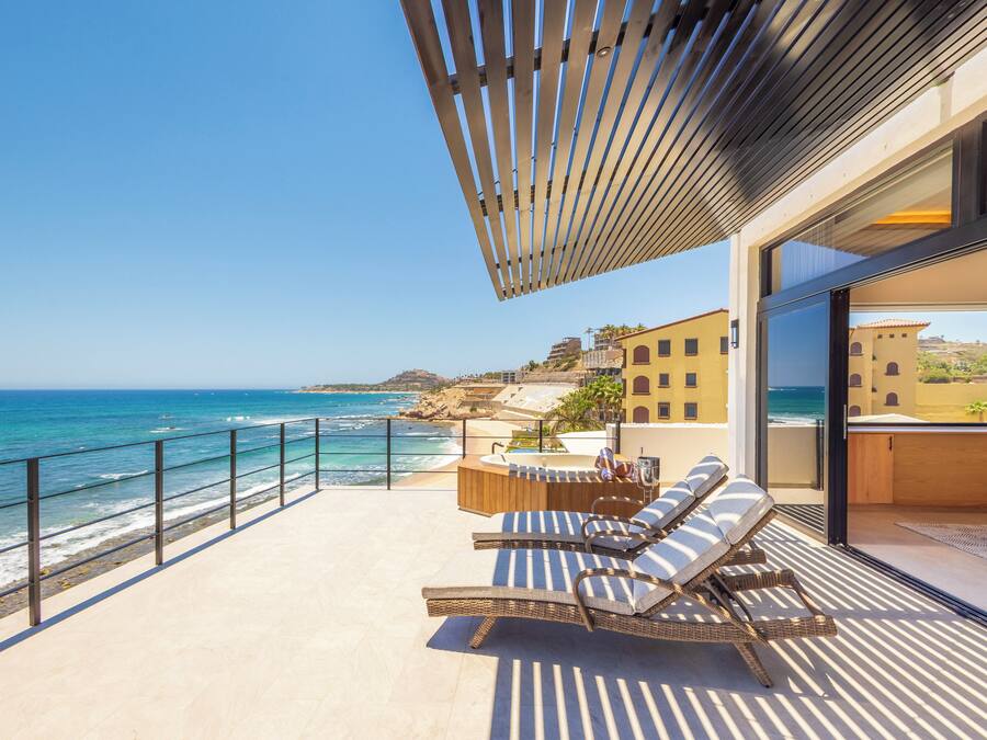 Un balcón con sillones de mimbre y una mesa de madera con vista a la playa y al océano.