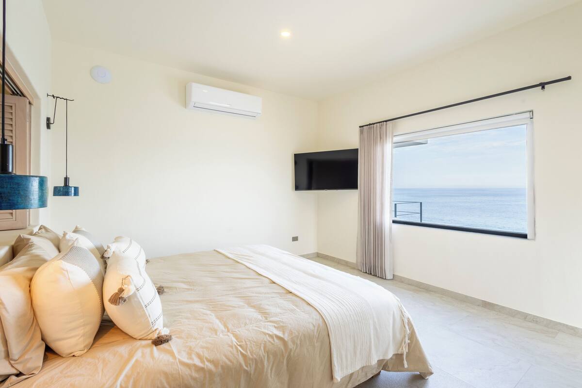 Une chambre dotée d’un grand lit, d’un téléviseur à écran plat, d’un appareil de climatisation et offrant une vue sur la mer par une fenêtre.