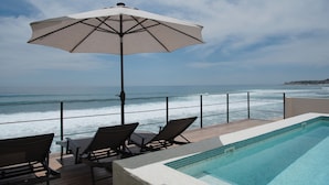 A poolside area with a view of the ocean, a lounge chair, a table, and an umbrella. - Cabo Break Hotel (San José del Cabo)