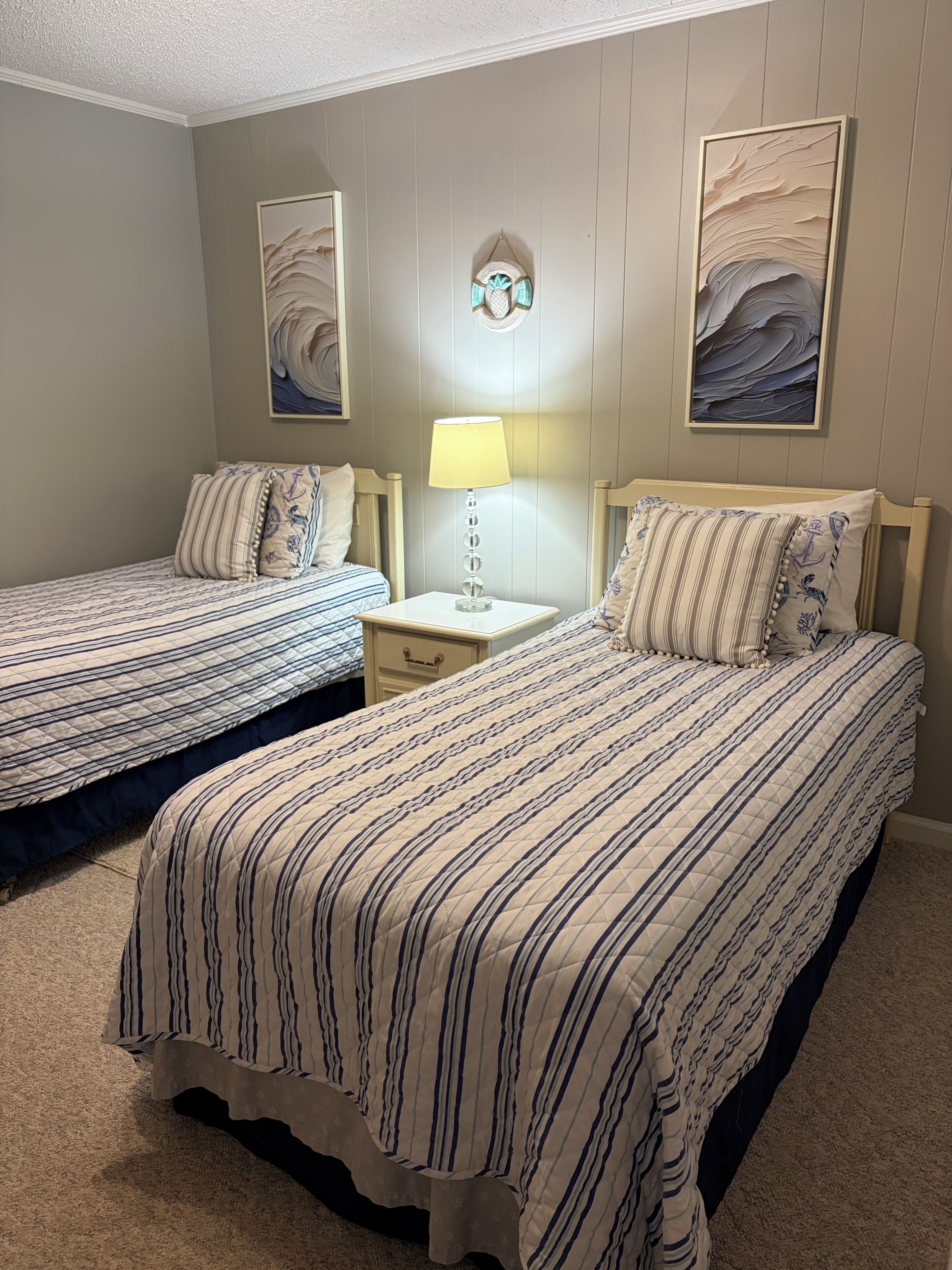 A bedroom with two beds, a nightstand, a lamp, and two wall art pieces.
