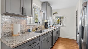A modern kitchen with grey cabinets, a granite countertop, and a stainless steel refrigerator. - The Drift House- Spacious Boho Family Retreat- 4 bds, 2 baths, 6 TVs, Movie Room (Clinton Township)