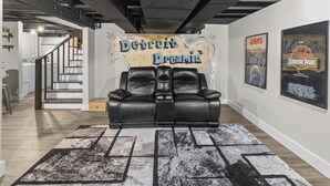 A room with a black leather sofa, a staircase, and posters on the walls. - The Drift House- Spacious Boho Family Retreat- 4 bds, 2 baths, 6 TVs, Movie Room (Clinton Township)