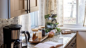 A kitchen with a coffee maker, a tray with jars, a book, and a window with curtains. - The Drift House- Spacious Boho Family Retreat- 4 bds, 2 baths, 6 TVs, Movie Room (Clinton Township)