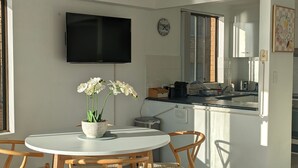 A modern kitchen with a flat-screen TV, a clock, and a window with a view of the outside. - Marine Parade - Ocean Views - Unit 6 (The Entrance)