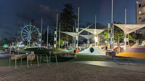 An outdoor public space with a Ferris wheel, modern architectural structures, and a paved area with benches.
