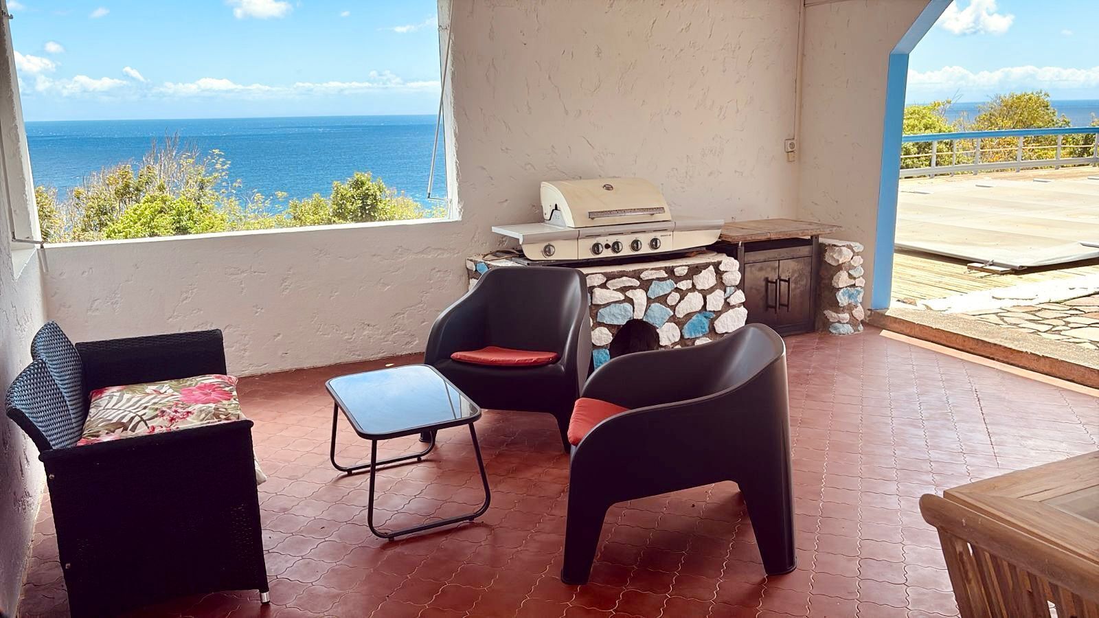Une pièce avec vue sur la mer, un barbecue, deux chaises et une petite table.