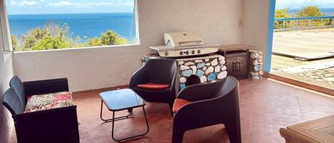 Une pièce avec vue sur la mer, un barbecue, deux chaises et une petite table.