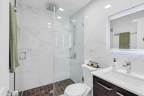 A modern bathroom with a glass-enclosed shower, a white toilet, a sink with a mirror, and a dark wooden cabinet.