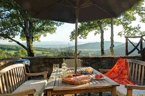 An outdoor dining area with a table set for two, a grill, and a scenic view.
