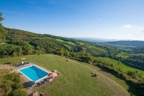A swimming pool with lounge chairs and an umbrella, surrounded by a grassy area with a view of rolling hills.