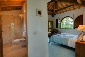 A bathroom with a shower, toilet, and sink. There is a bed with a window and a lamp.