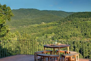 A terrace with a round wooden table and benches, surrounded by a metal railing, overlooking a forested valley. - Villa Torre Luna by MMega (Pieve Santo Stefano)