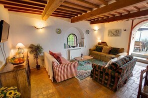 Ein gemütliches Wohnzimmer mit einem karierten Sofa, einem gemusterten Sofa, einem Couchtisch, einer Topfpflanze und einem Fenster voller Bücher.