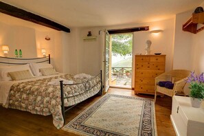 A bedroom with a bed, bedside lamps, a wooden dresser, a chair, and a view through an open door.