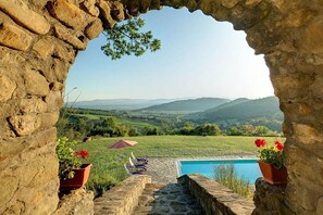 Ein Steinkreuzgang führt zu einem Poolbereich mit Blick auf sanfte Hügel.