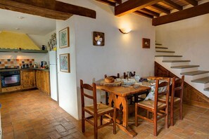 A rustic kitchen with a wooden table and chairs, a staircase, and a tiled backsplash. - Villa Torre Luna by MMega (Pieve Santo Stefano)