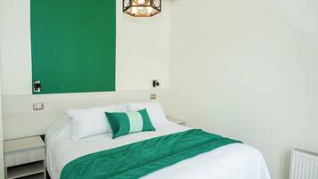 Un lit bien fait, recouvert d’une couvre-lit verte et blanche, agrémenté d’un plaid assorti, et surmonté d’un luminaire suspendu au design moderne.
