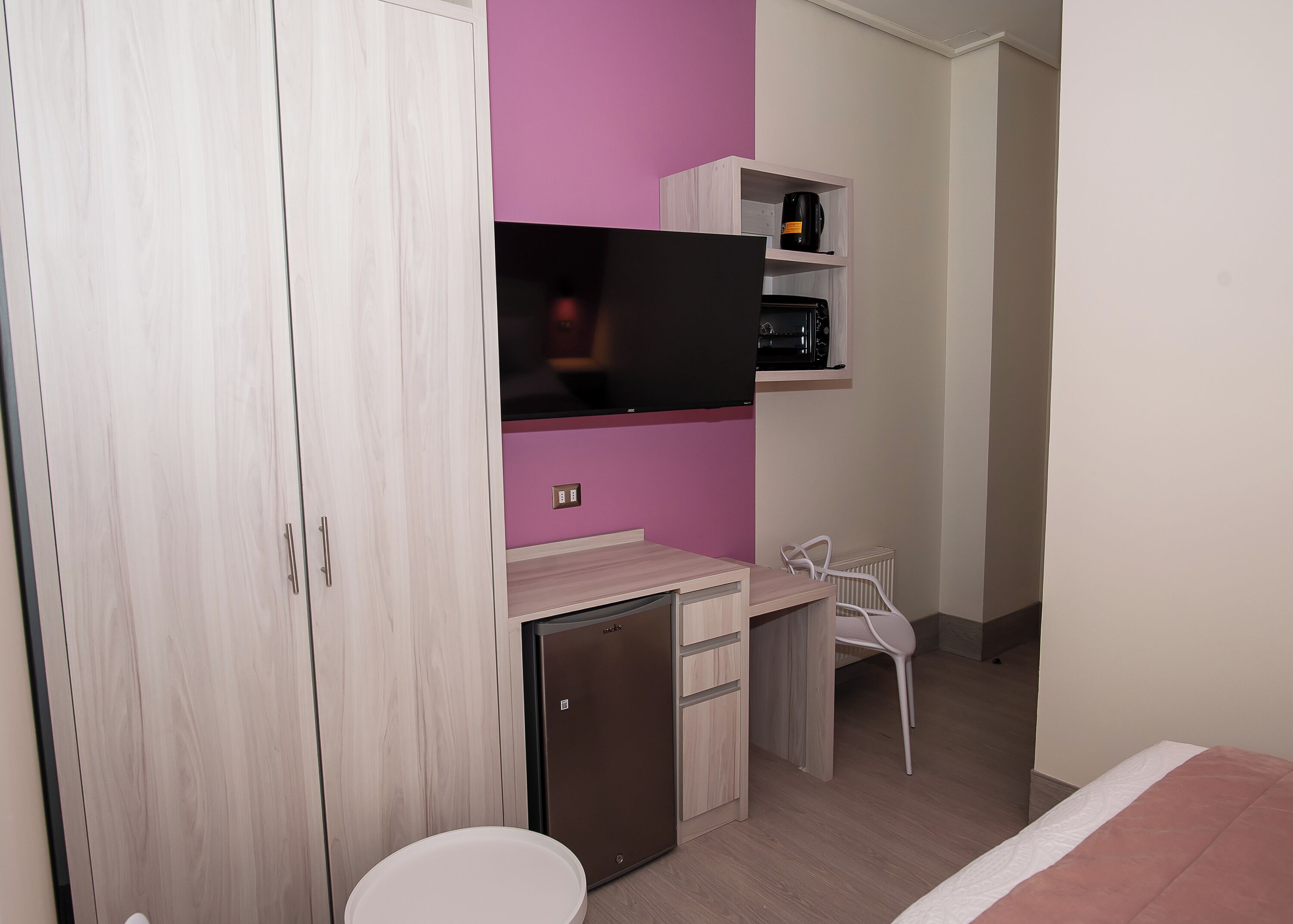 Un dormitorio con cama, escritorio con silla, televisión y armario.
