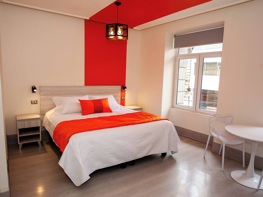 Un dormitorio moderno con cama, mesitas de noche, una ventana y una pequeña mesa redonda con una silla.