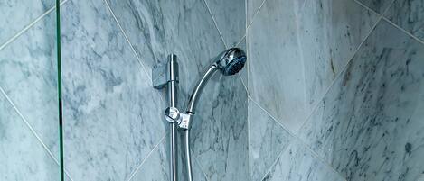 A shower with a handheld showerhead and a handheld scrubber, mounted on a wall with a marble tile pattern.
