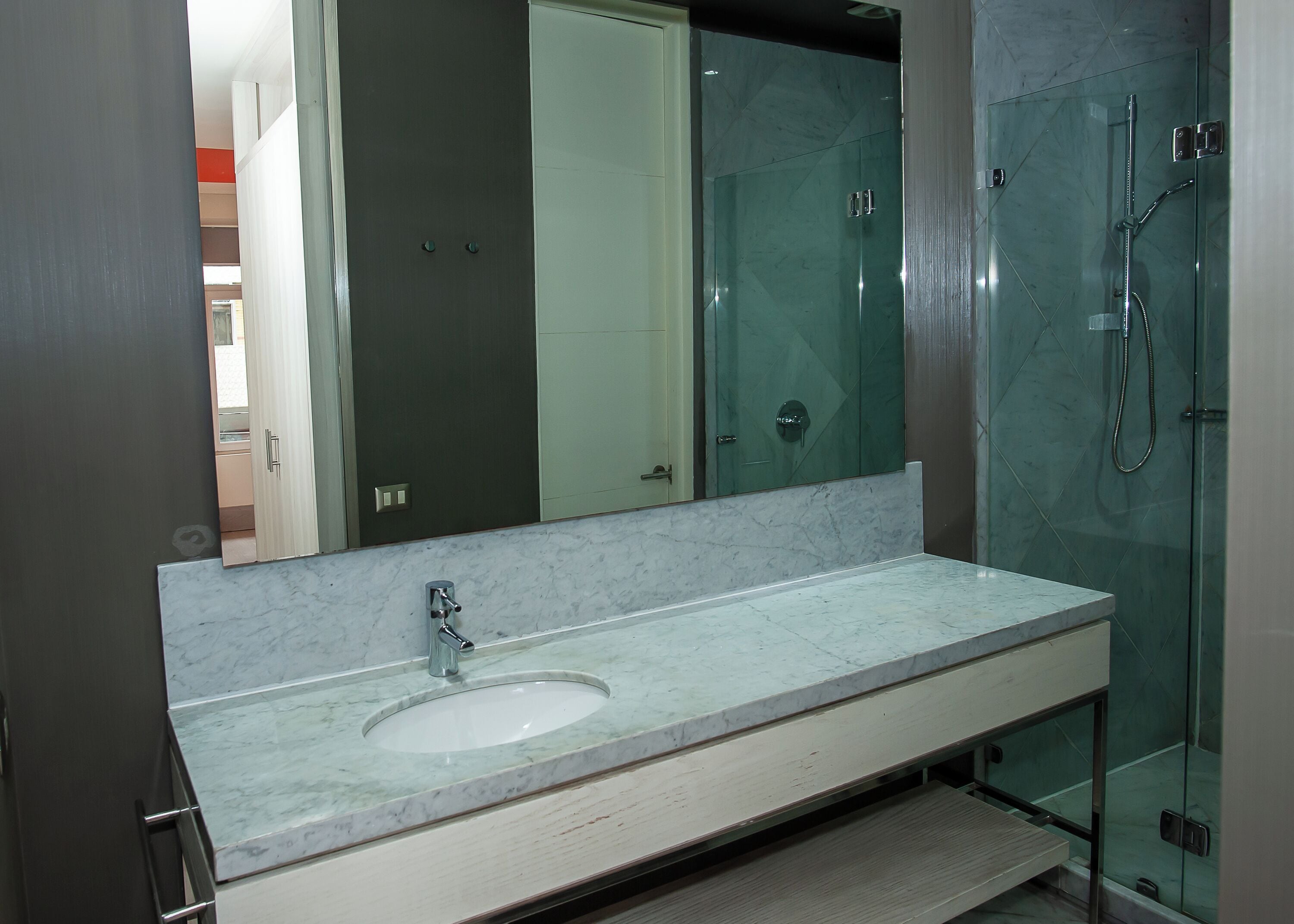 Un baño con lavamanos de mármol, cabina de ducha con mampara de cristal y un espejo grande.