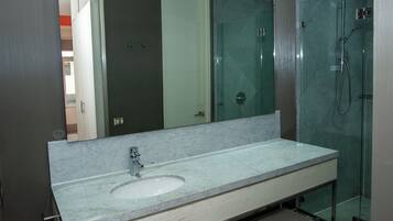 Un baño con lavamanos de mármol, cabina de ducha con mampara de cristal y un espejo grande.